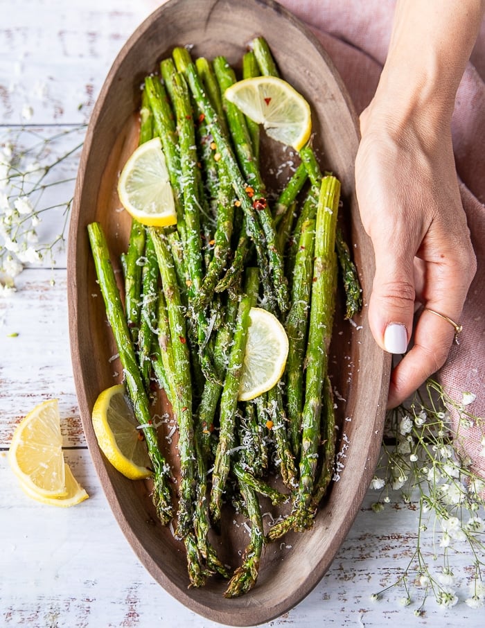 A hand holding a serving plate of Air Fryer Asparagus garnished with lemon slices