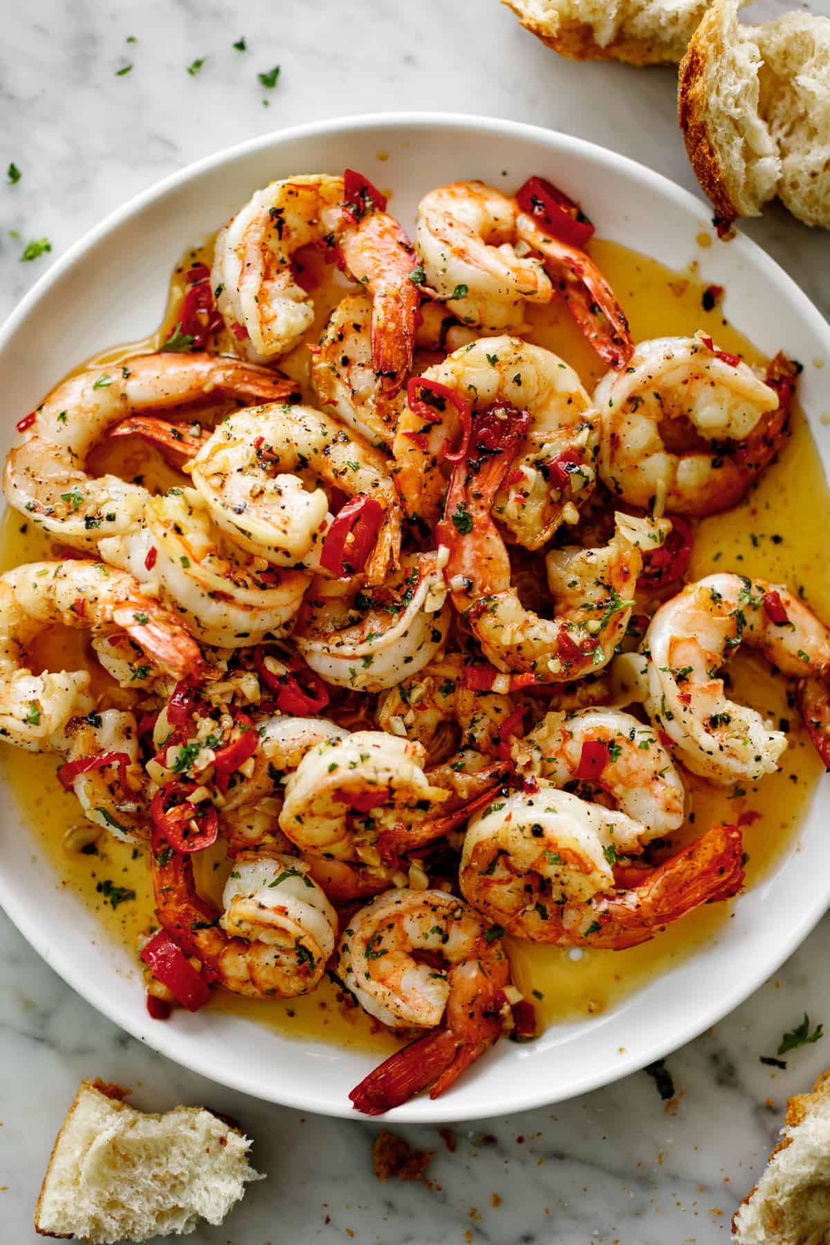 A pile of shrimp on a white plate sitting in chili garlic butter sauce. Served with broken bread pieces.