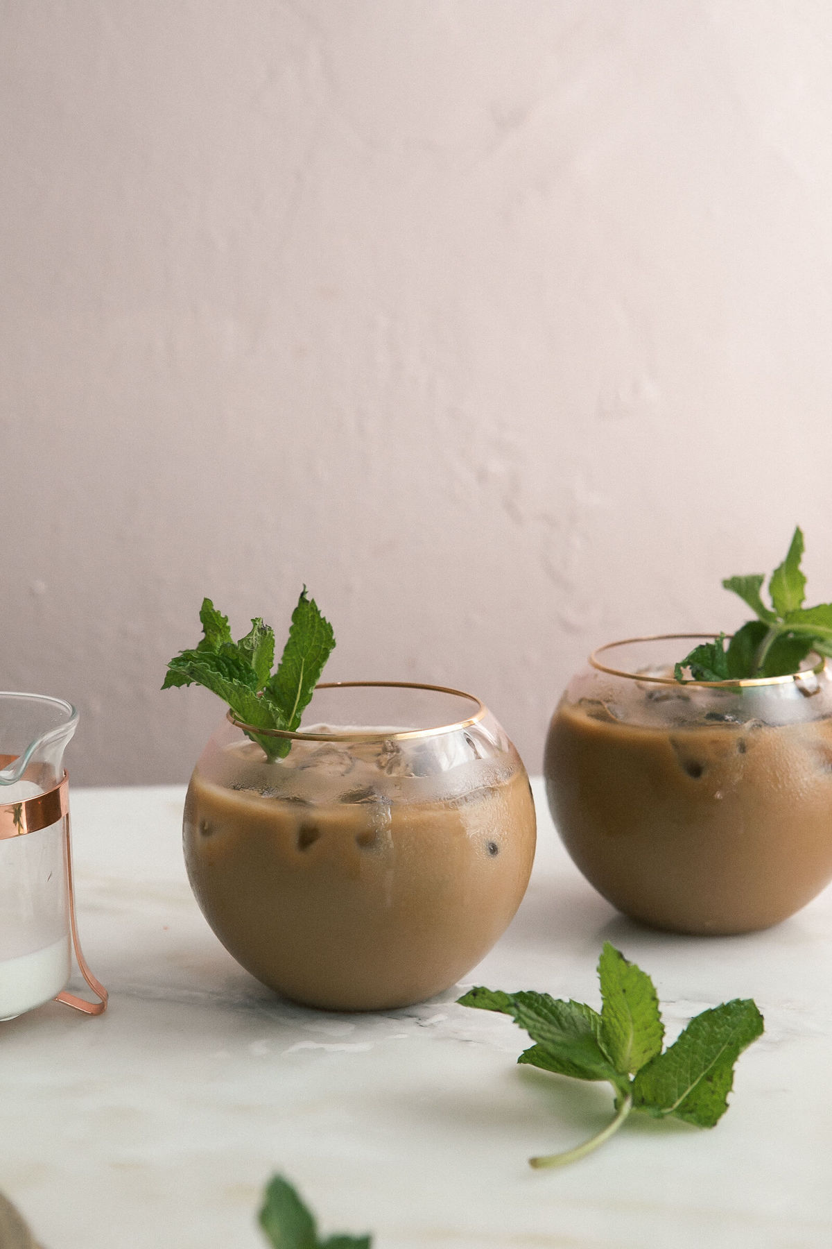 Mint Vanilla Iced Coffee in cups on a counter with fresh mint leaves.