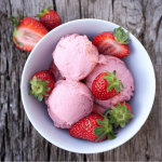 Overhead image of a white bowl with scoops of strawberry ice cream and fresh strawberries