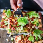 A hand holding a slice of sushi bake over a wooden tray using a spatula