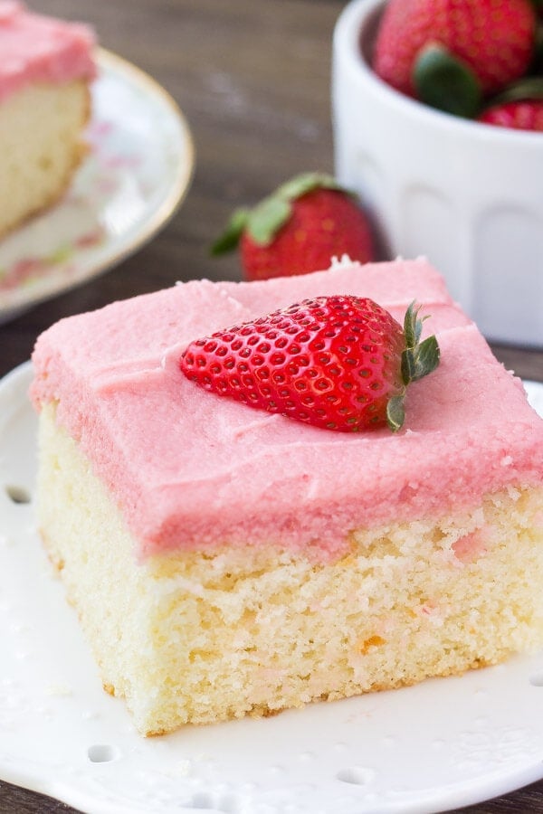 a photo of a piece of vanilla cake topped with pink strawberry buttercream and a half slice of fresh strawberry