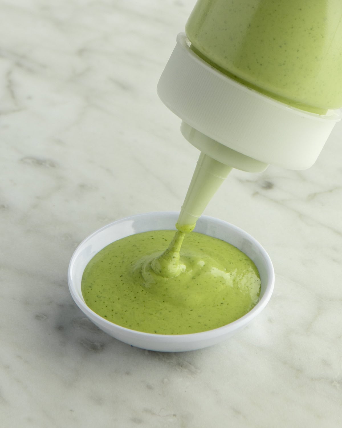 Aji Verde (Peruvian Green Sauce) being squeezed into a dish.