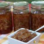 Autumn colored table cloth with white dish of onions and honey sauce, three pint jars of canned onions in the background.