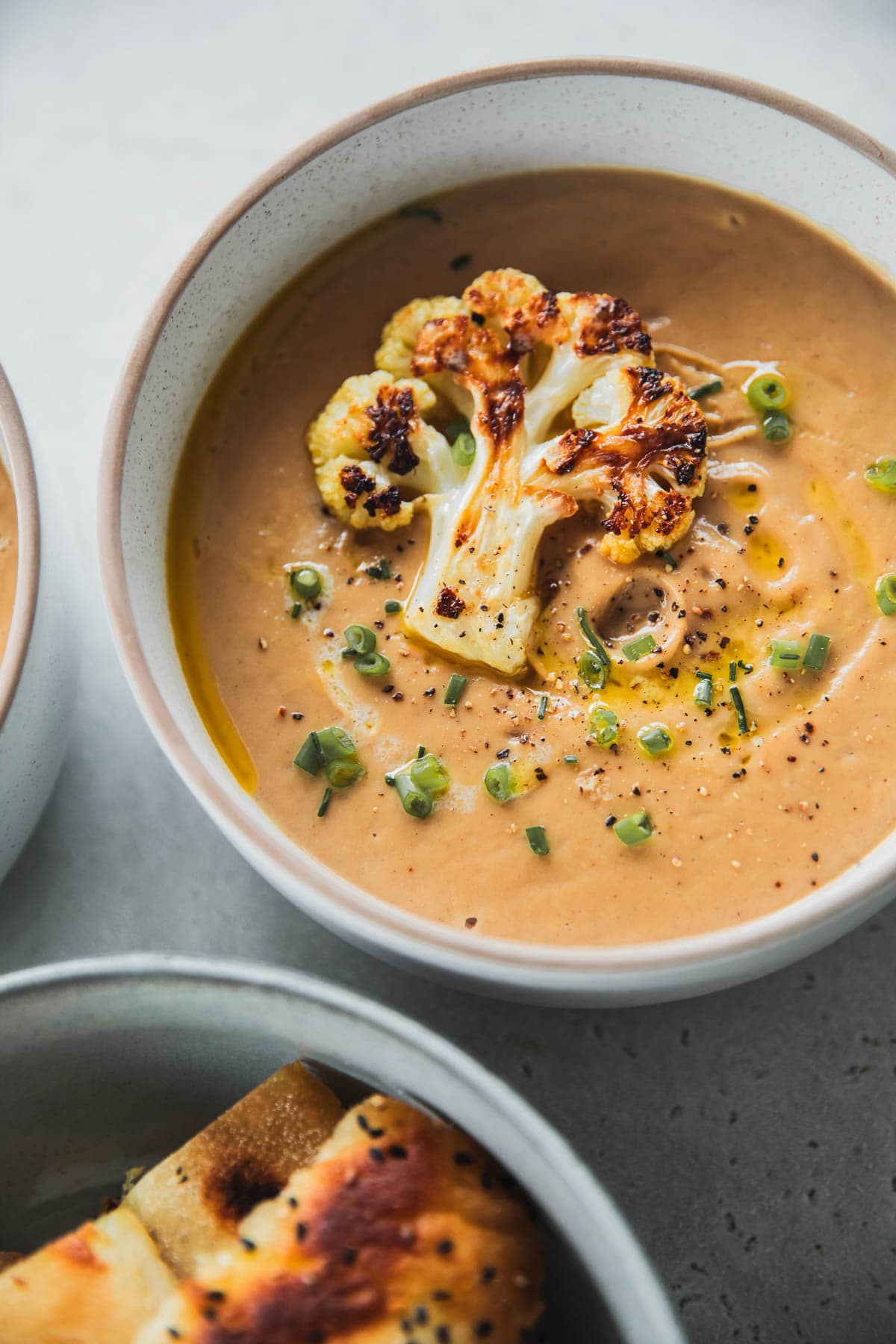 Roasted Cauliflower Soup in a bowl with cauliflower floret garnish and toasted bread.