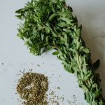 bundle of fresh mexican oregano and some dried mexican oregano on a white marble surface.