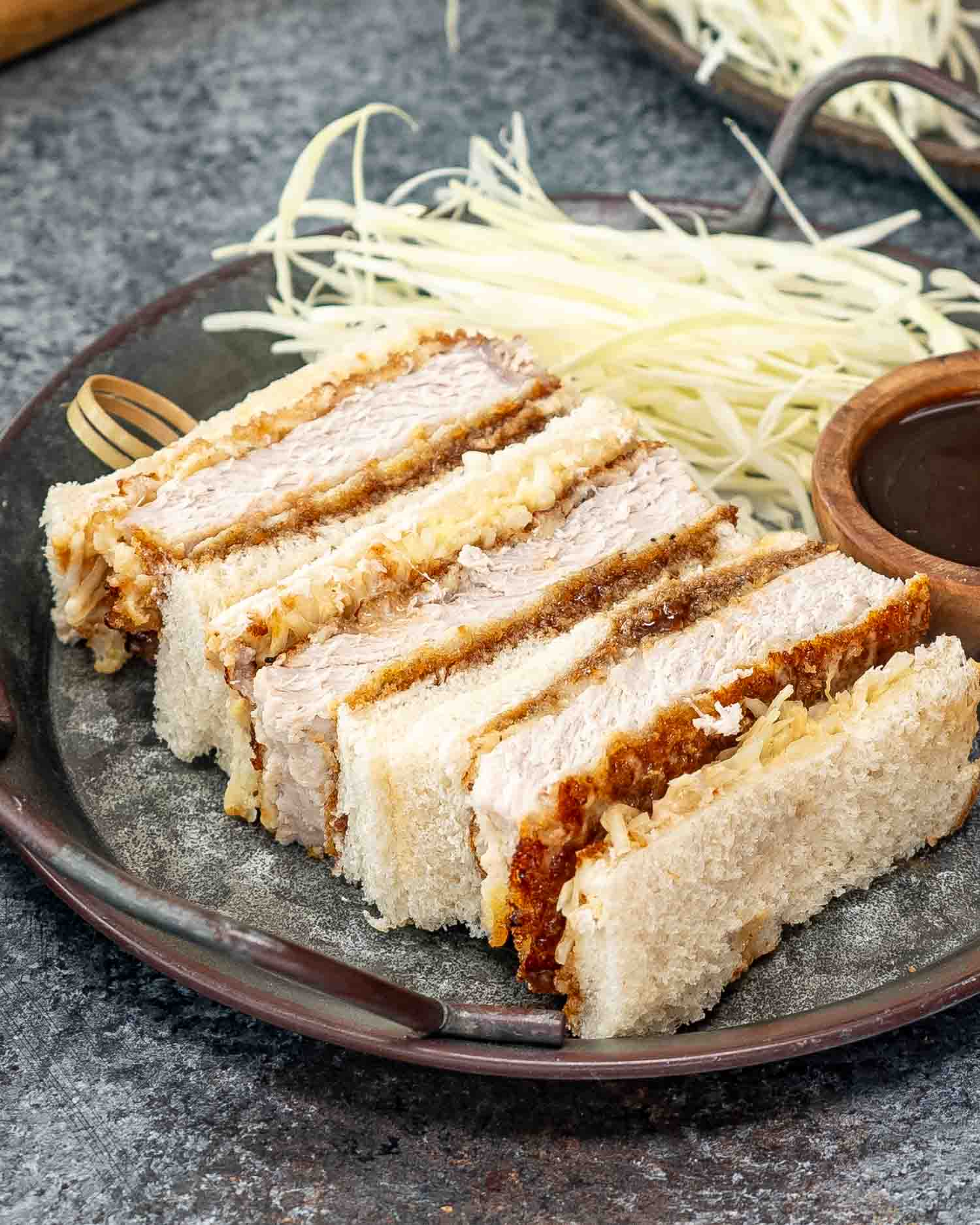 katsu sando on a metal plate with tonkatsu sauce in a bowl and cabbage.