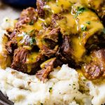 A photo of beef short ribs smothered in mustard Carolina BBQ sauce over a pile of mashed potatoes.