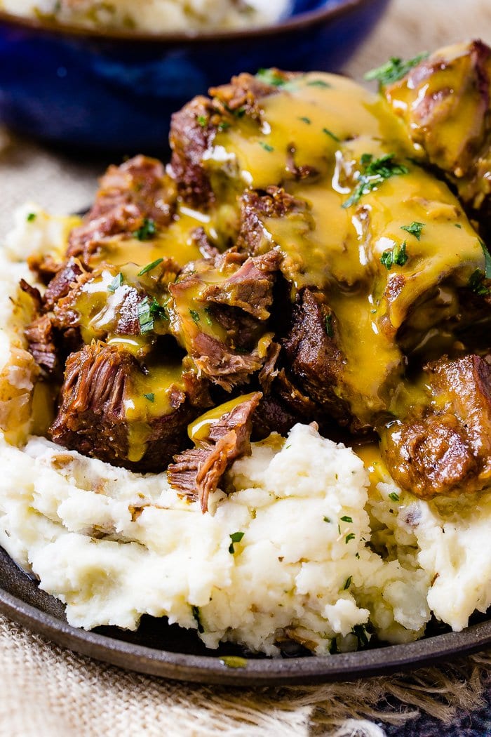 A photo of beef short ribs smothered in mustard Carolina BBQ sauce over a pile of mashed potatoes.