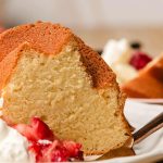 Slice of vanilla pound cake on a white plate with strawberries and whipped cream.