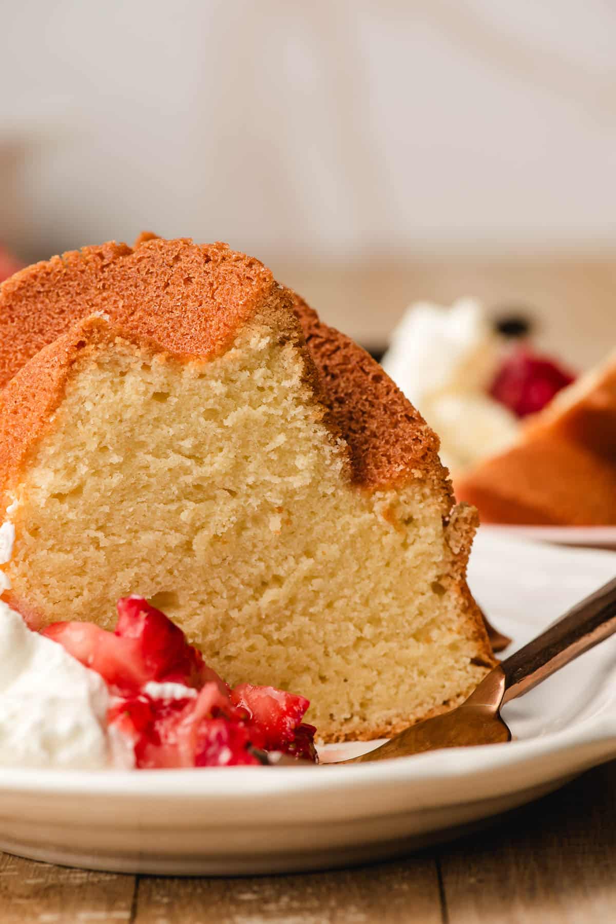 Slice of vanilla pound cake on a white plate with strawberries and whipped cream.