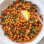 Sauteed Spicy Chickpeas in a white bowl with a lemon wedge and spoon.