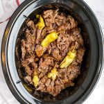 cooked mississippi pot roast shredded in a slow cooker with pepperoncini on top