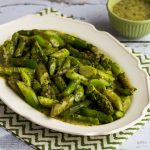 Square image for Asparagus with Basil Vinaigrette shown on platter on green-white napkin with basil vinaigrette on the side.