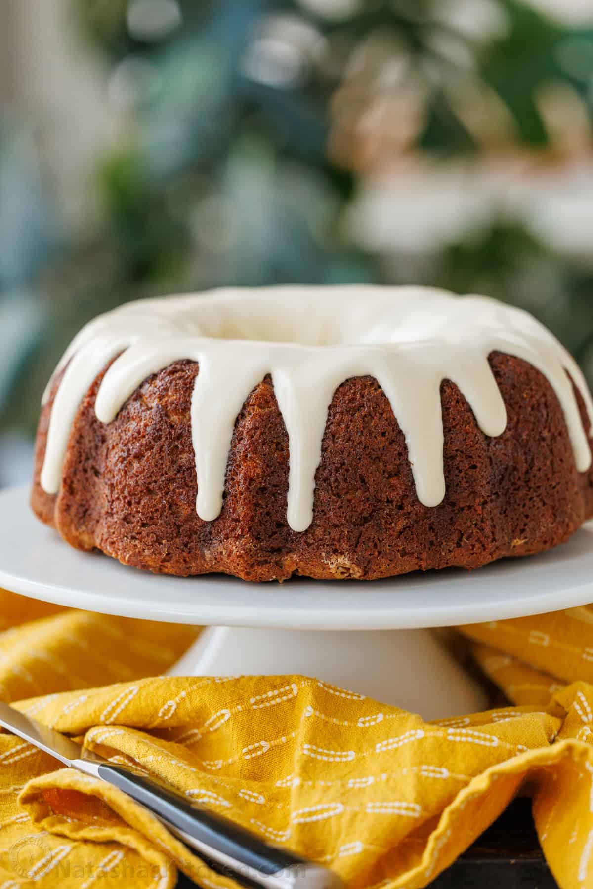 Iced Banana Bundt Cake with a yellow table cloth and knife for cutting