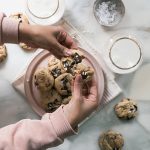 Hands breaking Bourbon Pecan Chocolate Chip Cookies in half.