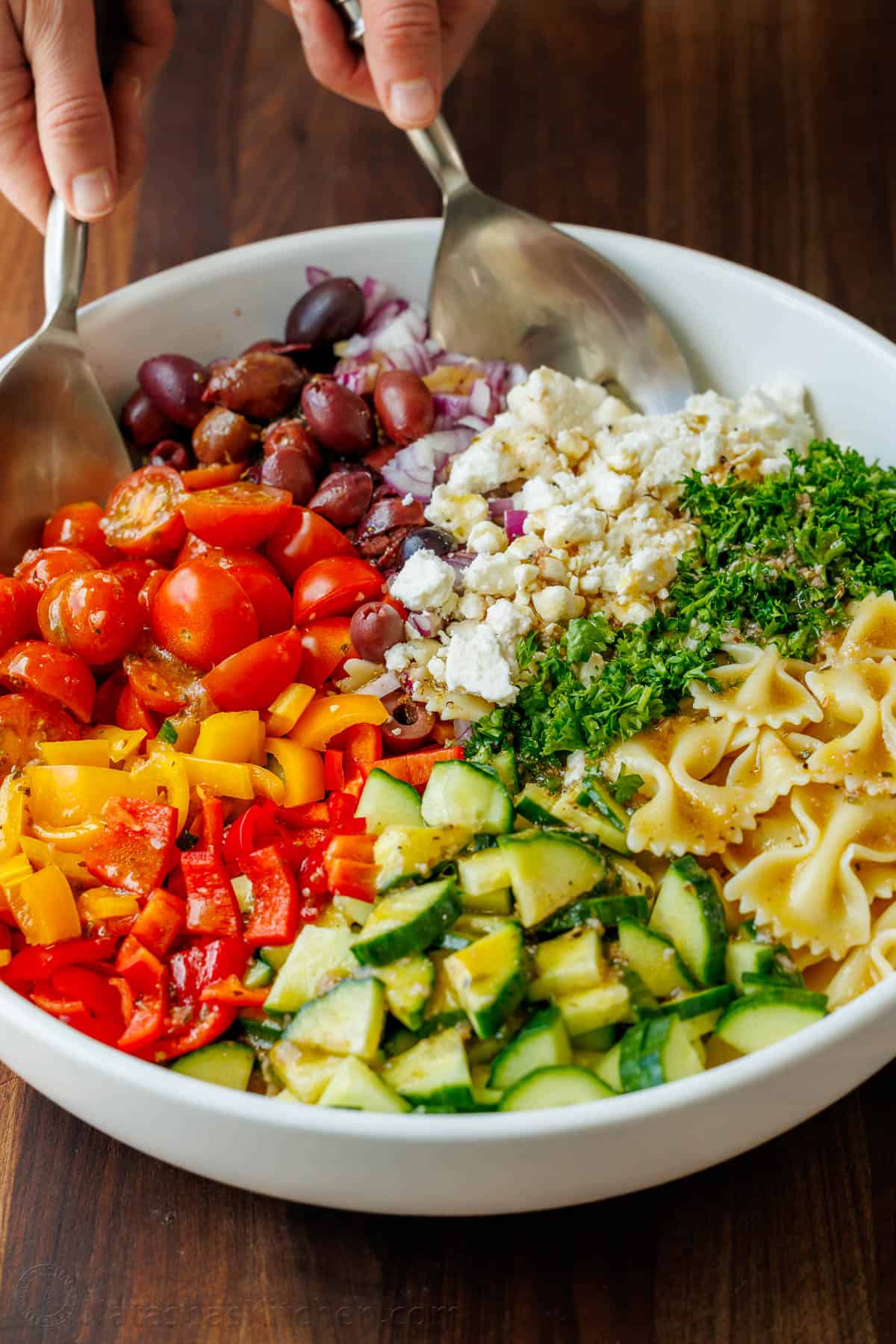 Greek Pasta Salad ingredients being tossed in a white serving dish