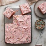 Strawberry Sheet Cake with Rhubarb Frosting sliced topped with sprinkles.