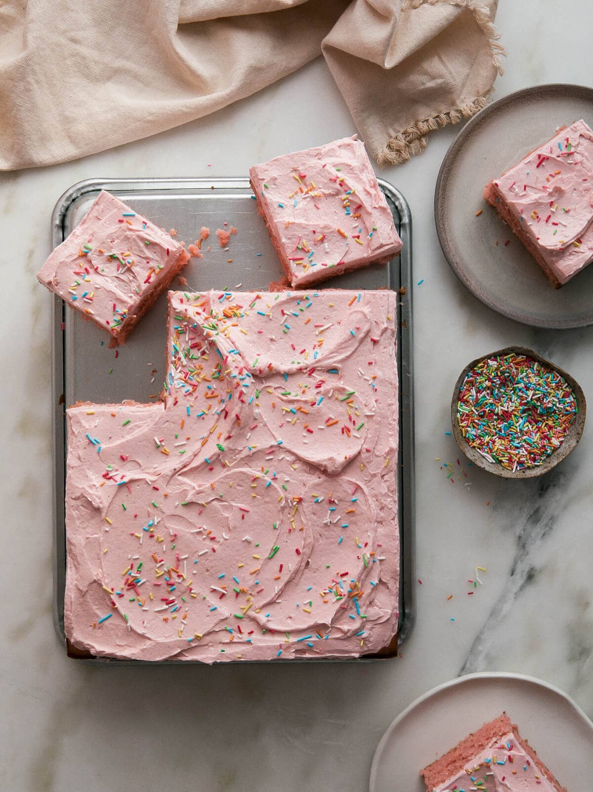 Strawberry Sheet Cake with Rhubarb Frosting sliced topped with sprinkles.