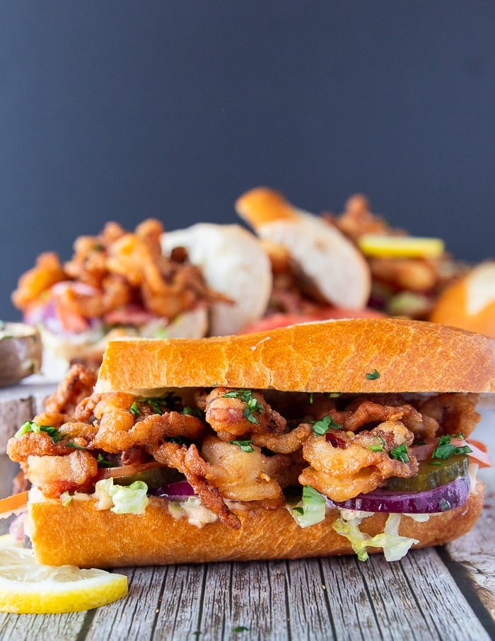 close up on a po boy sandwich cut in half , showing up close the fried shrimp and the sandwich toppings along with the sauce dripping on the sides of the bread