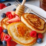 Sourdough discard pancakes stacked on a plate with fresh berries and drizzled honey