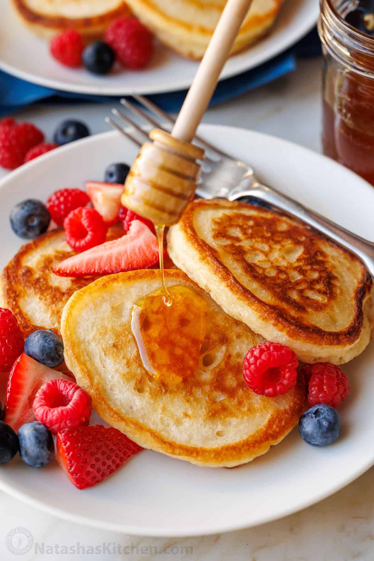 Sourdough discard pancakes stacked on a plate with fresh berries and drizzled honey