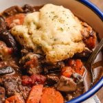 Dumpling topped beef stew in a bowl with a blue rim.