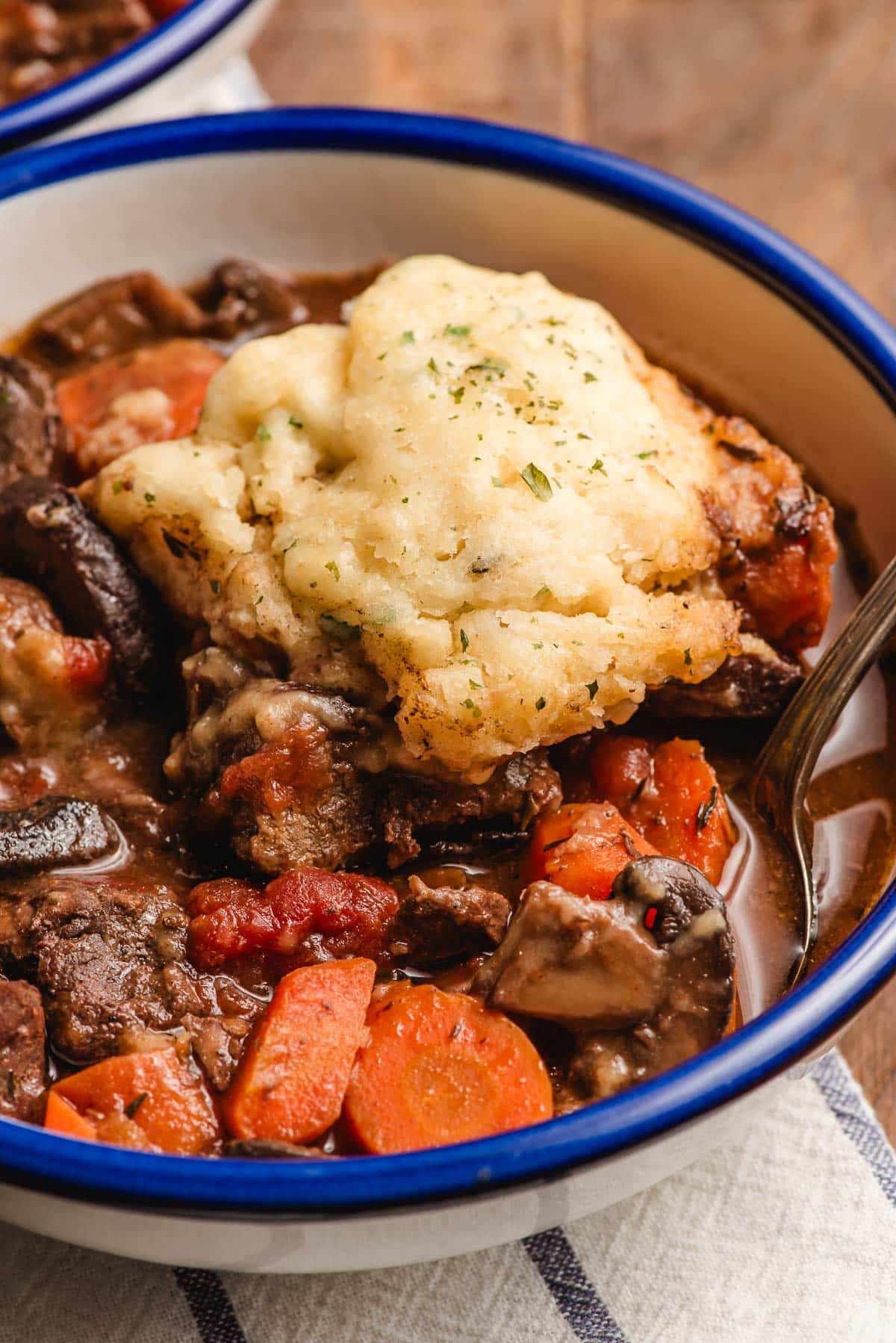 Dumpling topped beef stew in a bowl with a blue rim.