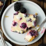 a photo of a blackberry lime bar sitting on a small plate with a corner scooped off by a fork sitting on the plate next to it.