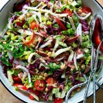 A classic chopped salad in a large salad bowl with tongs.