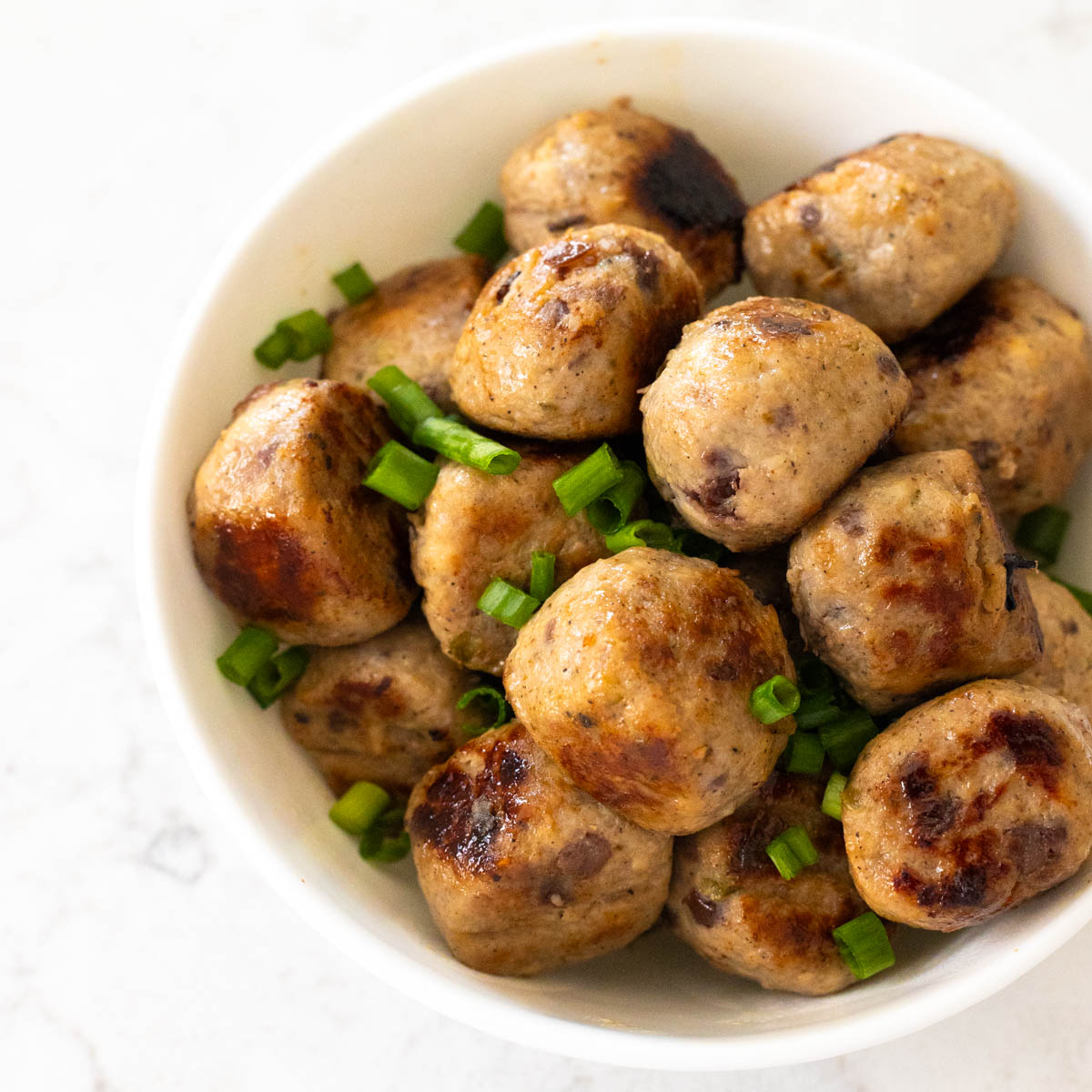 A white bowl filled with cranberry jalapeño meatballs has chopped green onions sprinkled over the top for garnish.