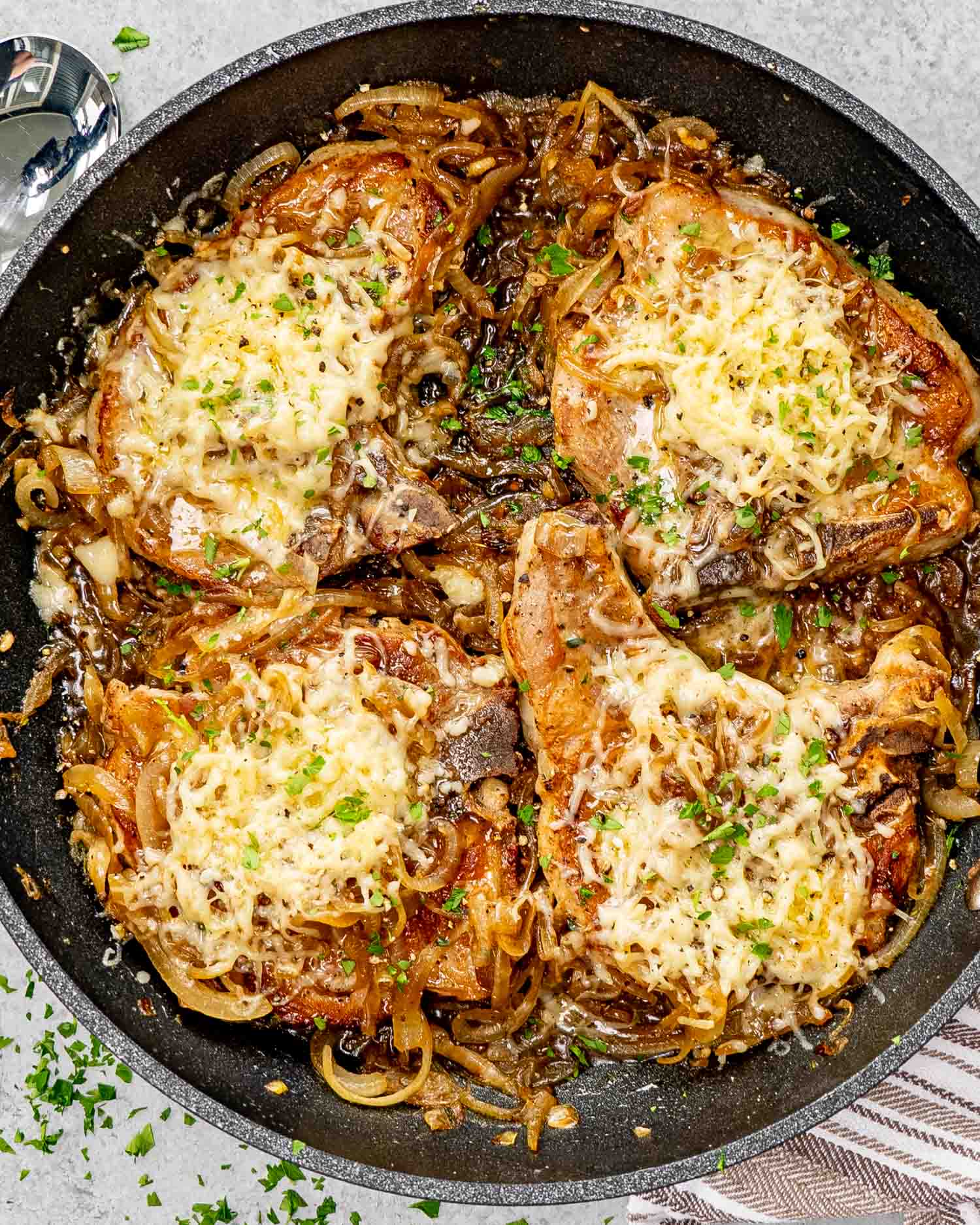 French onion pork chops in a skillet garnished with fresh thyme and parsley.