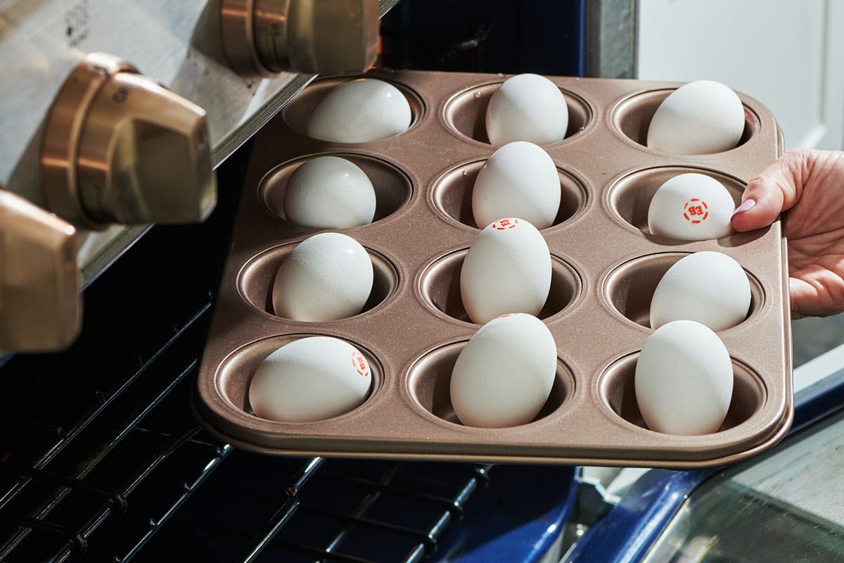 Placing muffin tin of raw eggs in oven for hard-boiled eggs.