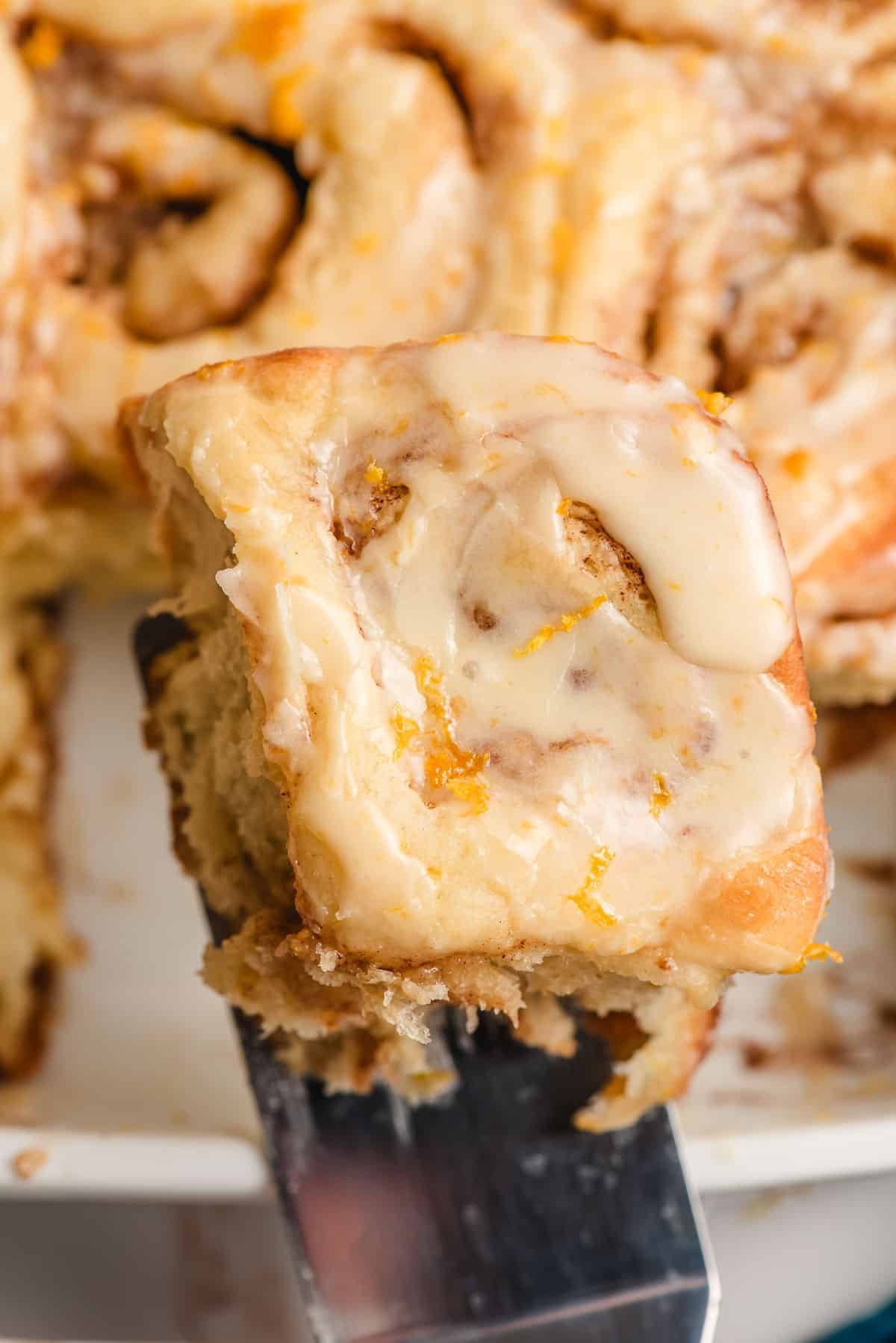 Spatula lifting an orange roll from a casserole dish.