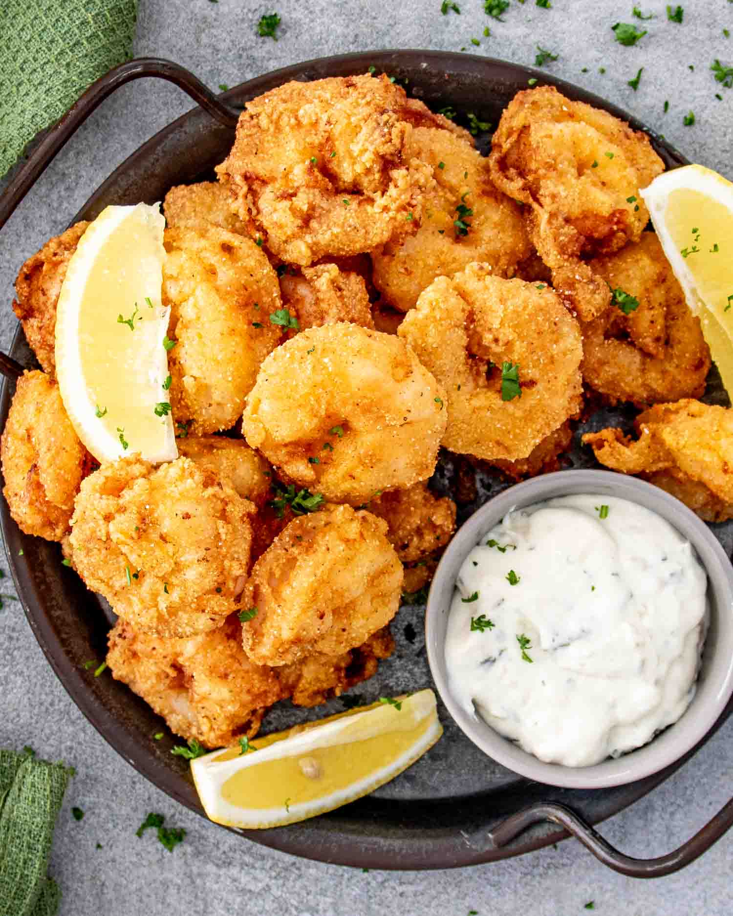 popcorn shrimp on a platter with a little bowl with tartar sauce and garnished with lemon wedges.