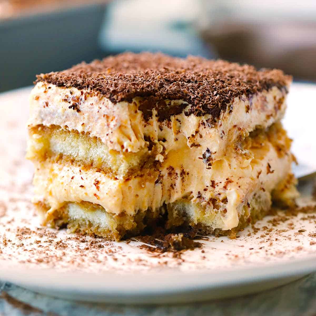 Square photo of a slice of pumpkin chai tiramisu taken from the side showing the layers and a bite taken out with a fork.